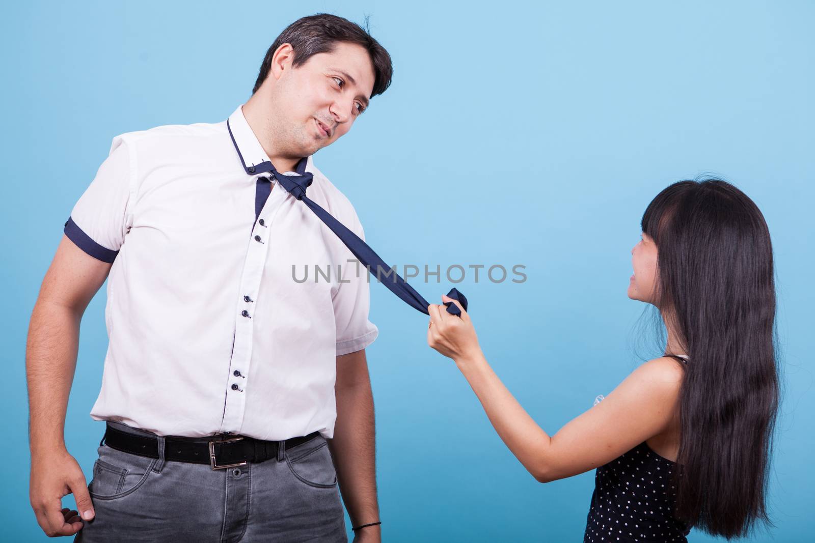 Playful asian girlfriend pulling her boyfriend tie. Intrracial couple.