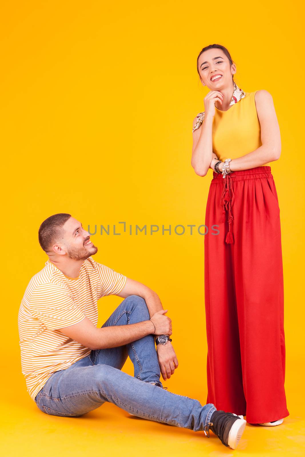 Girl smiling to the camera in studio over yellow background and boyfriend lookin up at her.