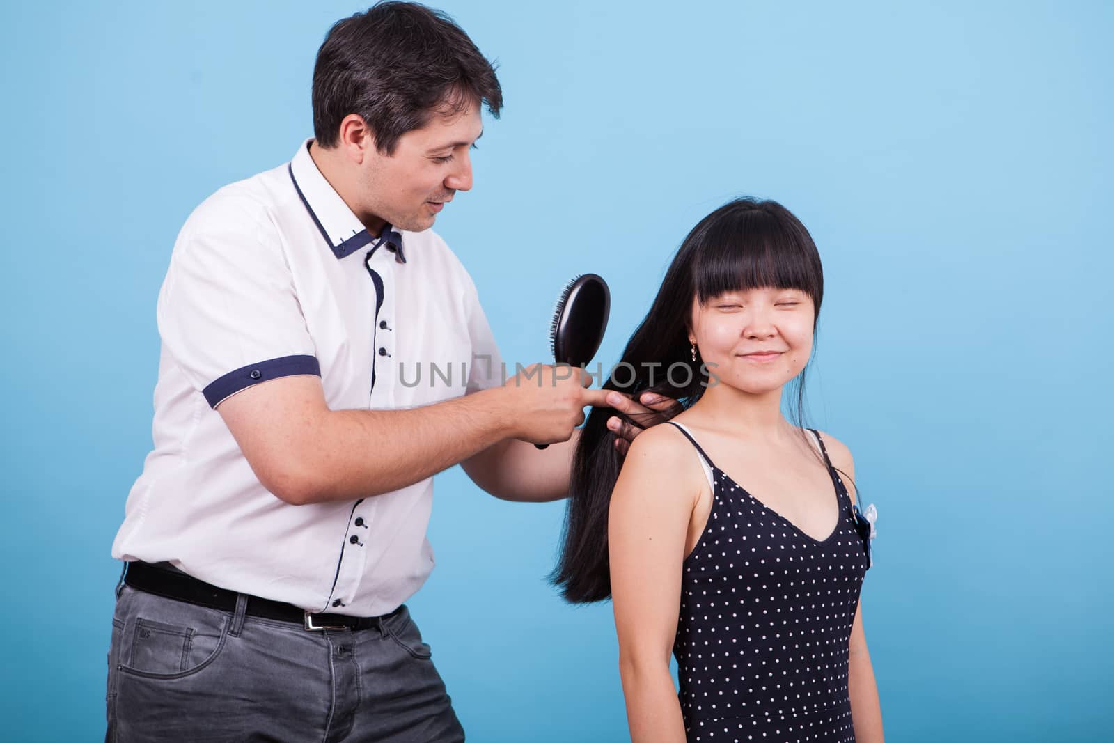 Caucasian boyfriend brushing his girlfriend hair in studio. Asian girlfriend smiling.