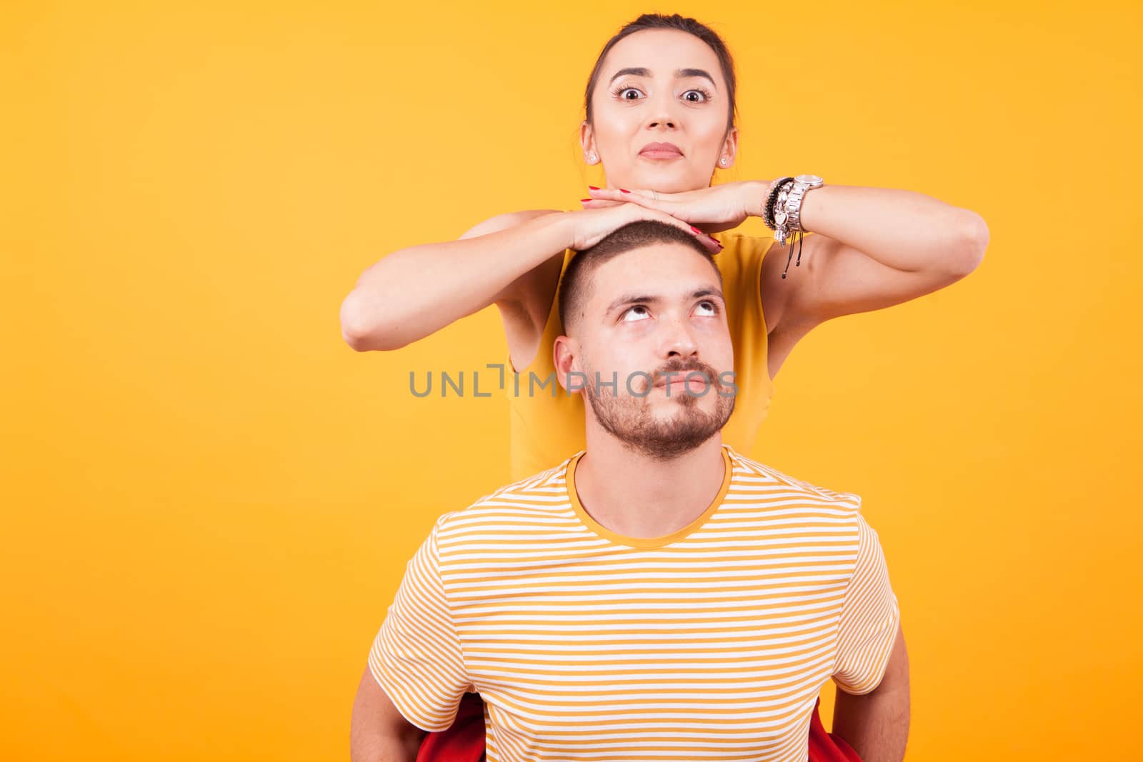 Beautiful couple having fun while man piggybacking his girlfriend in studio over yellow background.