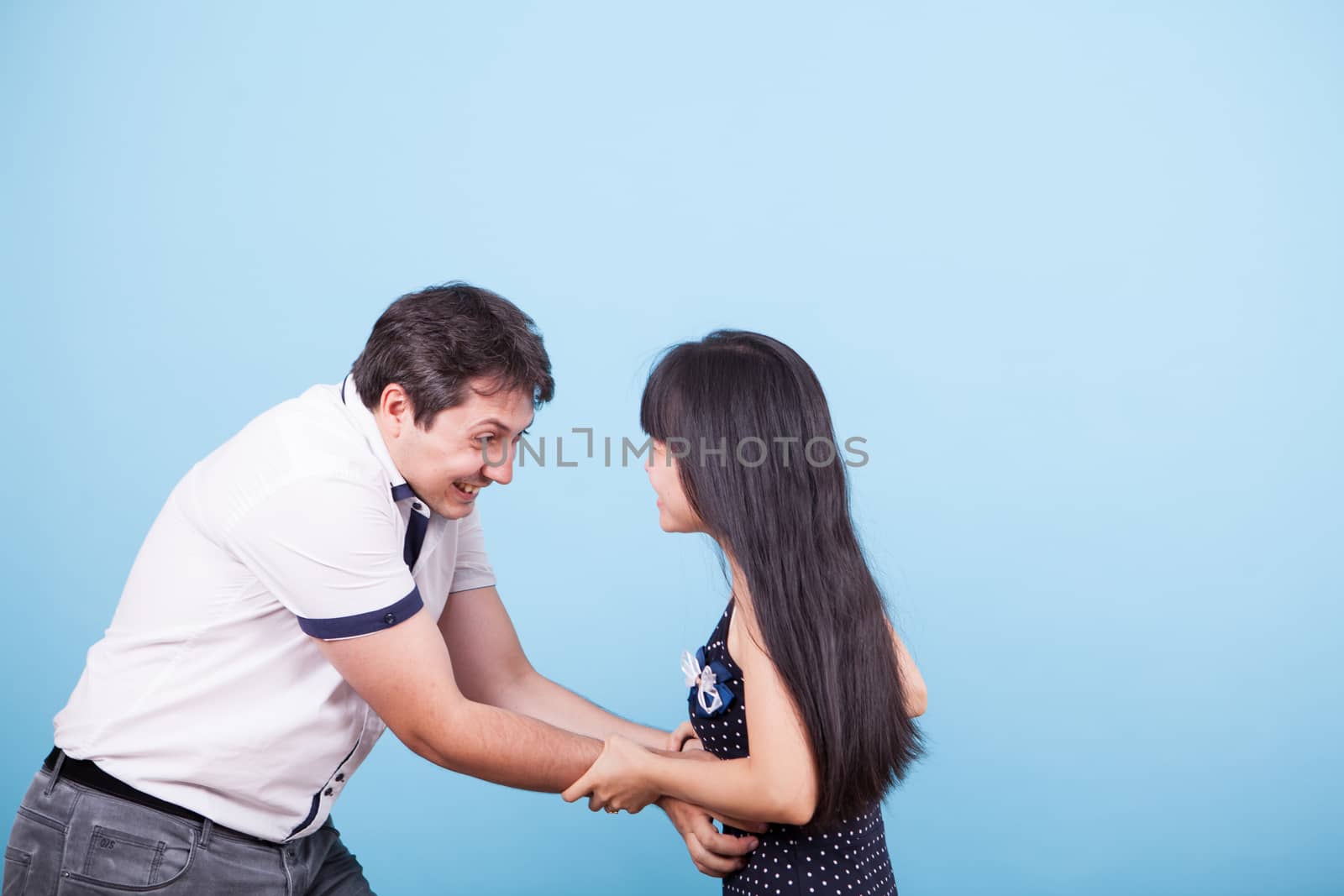 Caucasian boyfriend tickling his asian girlfriend in studio. Happy relationship between interracial couple.