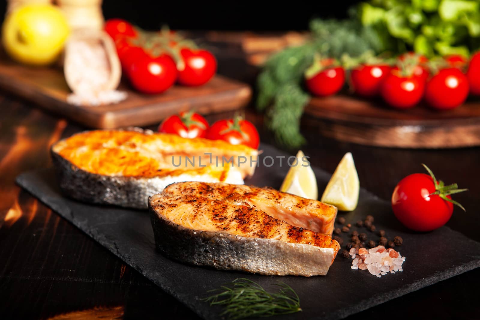 Grilled salmon rings placed on a stone platter. Salt and tomatoes in the background