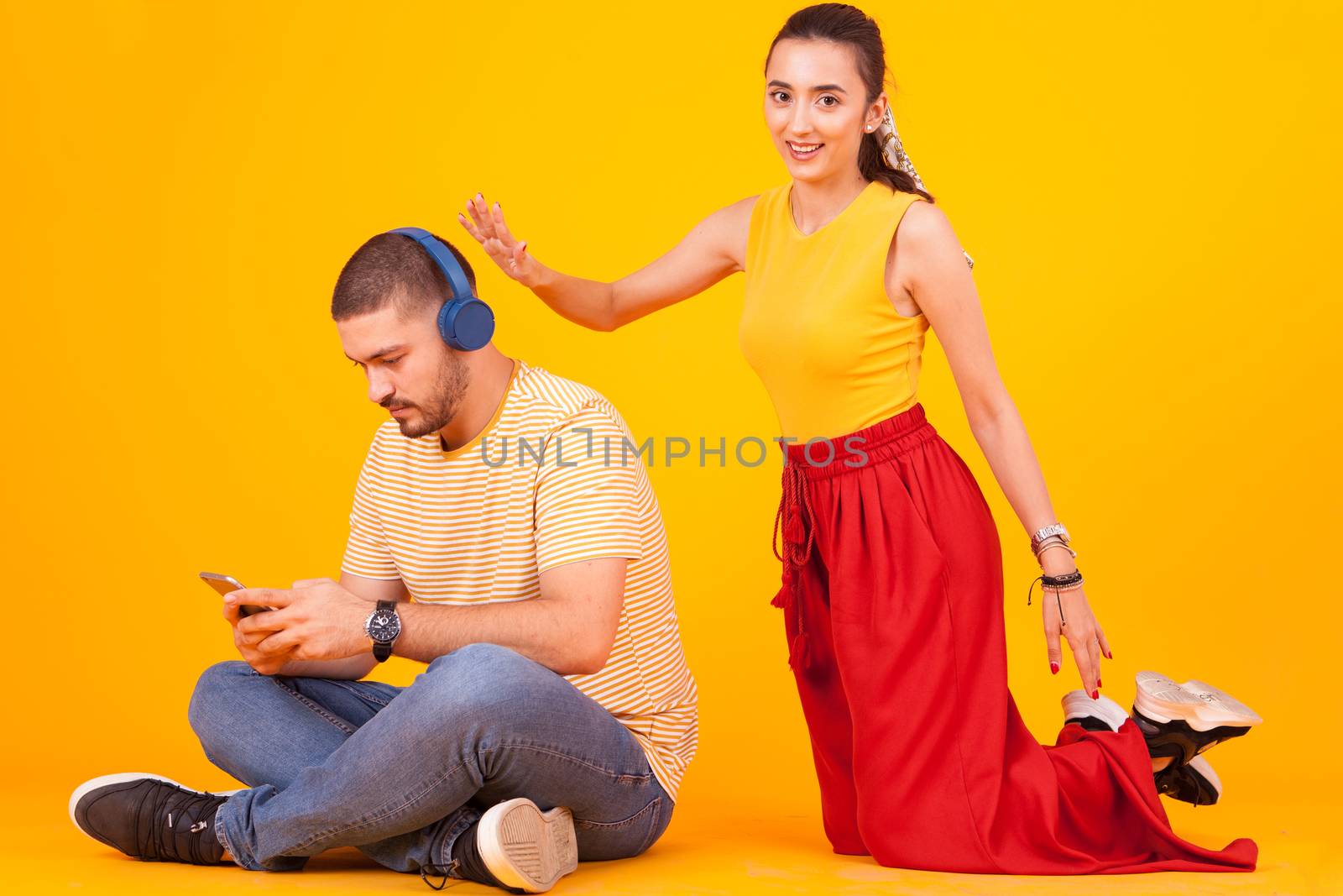 Boyfriend using his phone while girlfriend trying to get his attention. Couple sitting on studio floor.