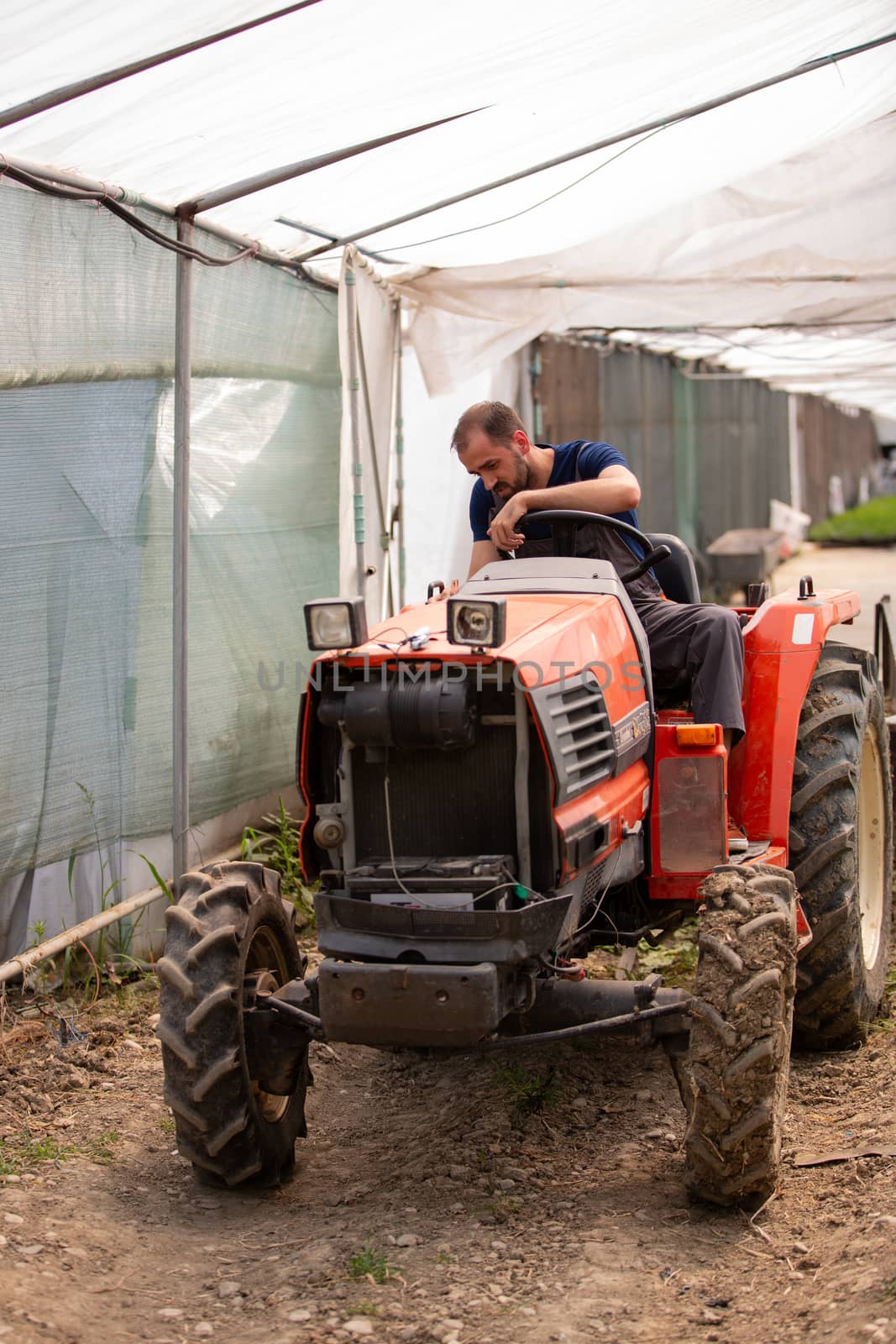 Young farmer trying to start a tractor in a greenhouse. Rural activity