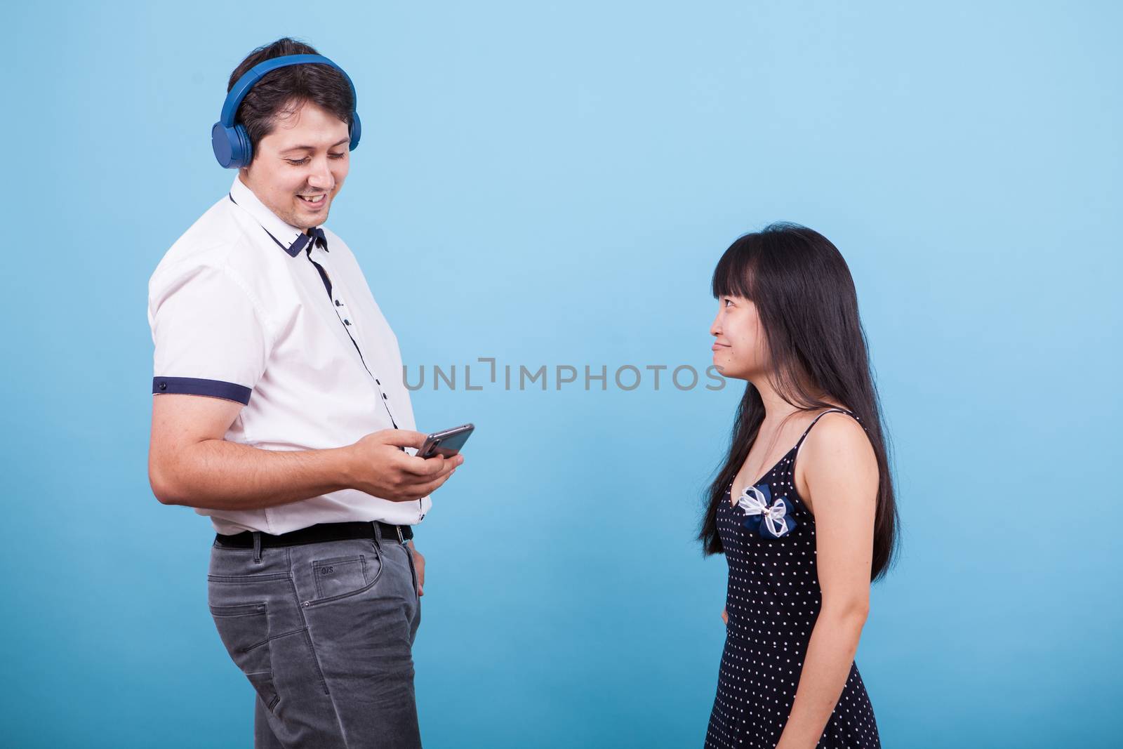 Smiling caucasian boyfriend with headphones ignoring his asian girlfriend. Interracial couple.