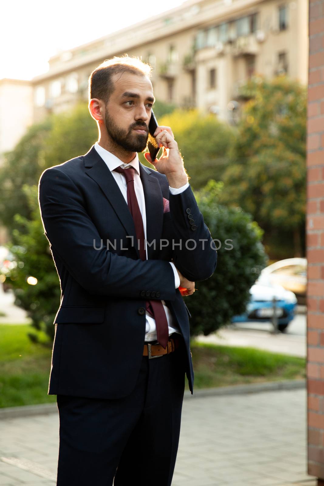 Caucasian businessman talking on the phone at sunset in the city. Business style and street view