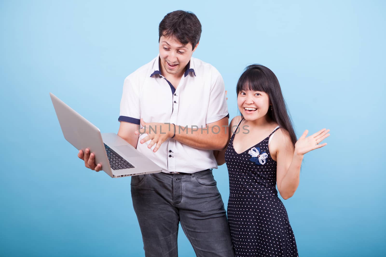 Caucasian husband showing his asian wife something exciting on laptop in studio. Interracial couple.
