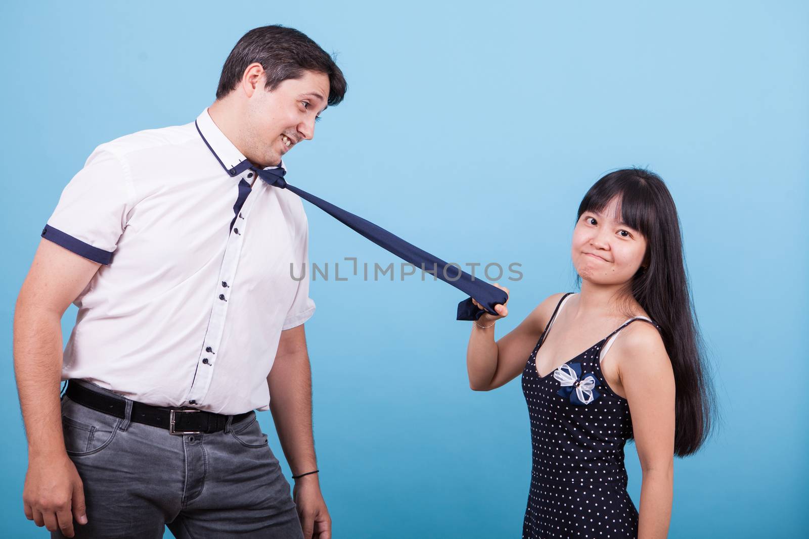 Angry asian girlfriend pulling her caucasian boyfriend tie. Interracial couple.