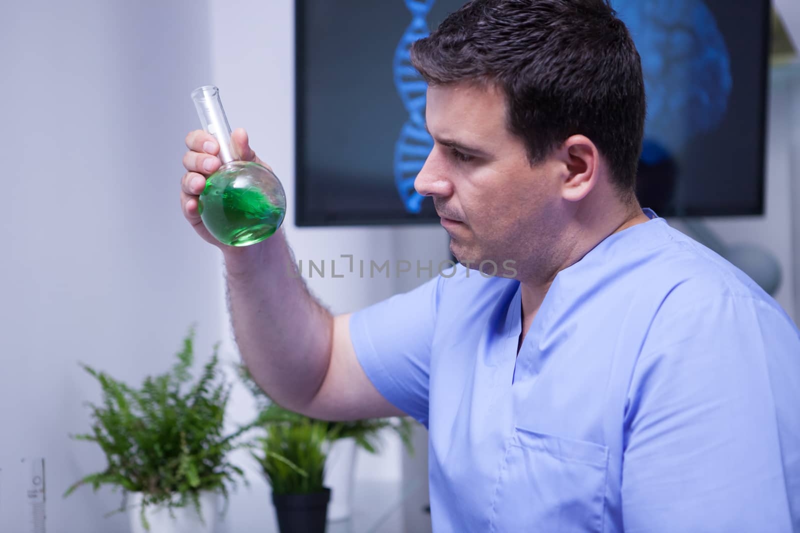 Young male scientist in uniform looking at a green solution in a test tube. Science in human health.