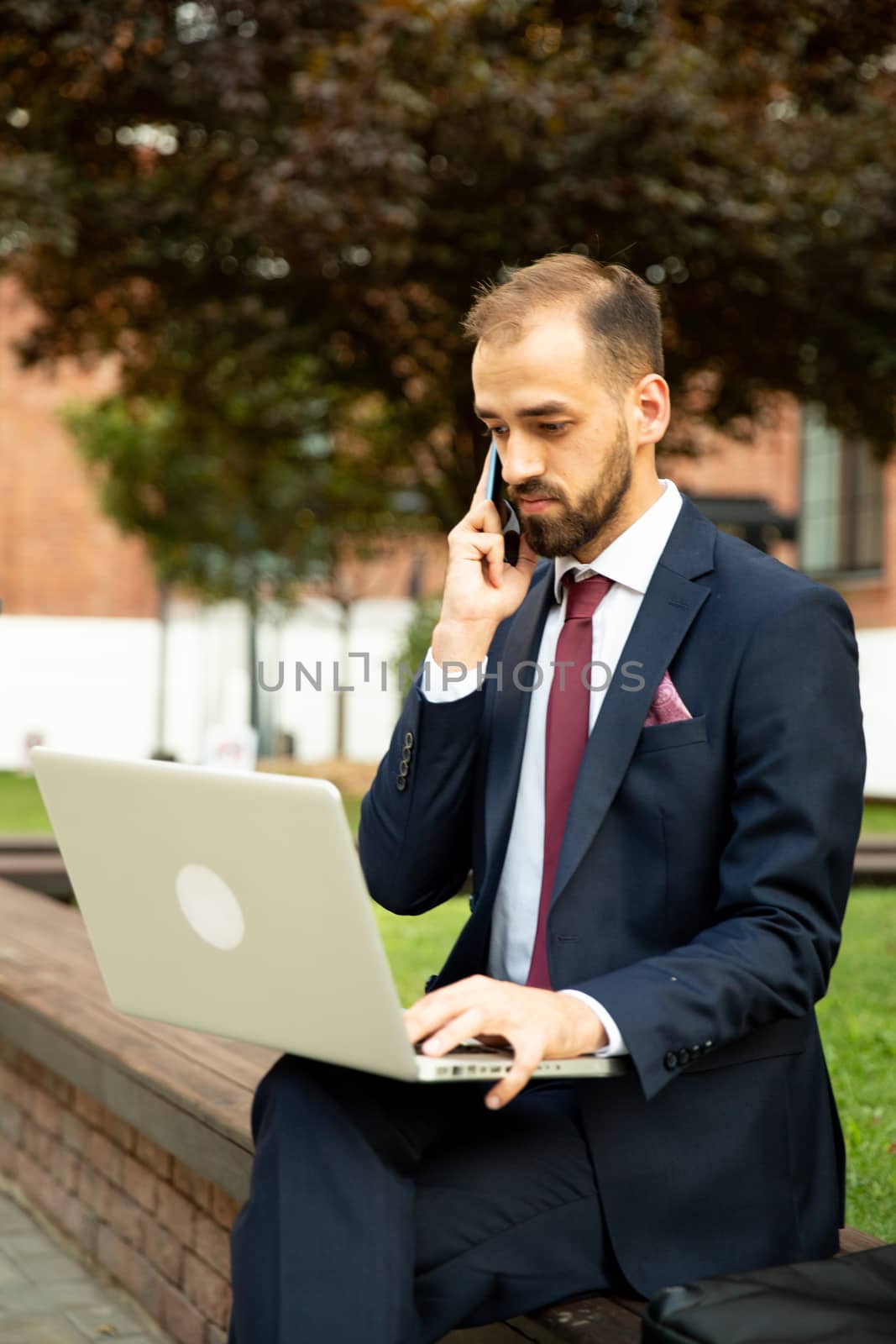 Business man talking on the phone and working on the laptop outside. Business style and professional attitude