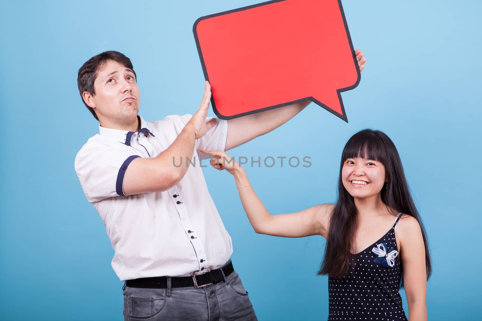 Asian girlfriend pointing at his caucasian boyfriend while he is holding an empty sign. Interracial couple.