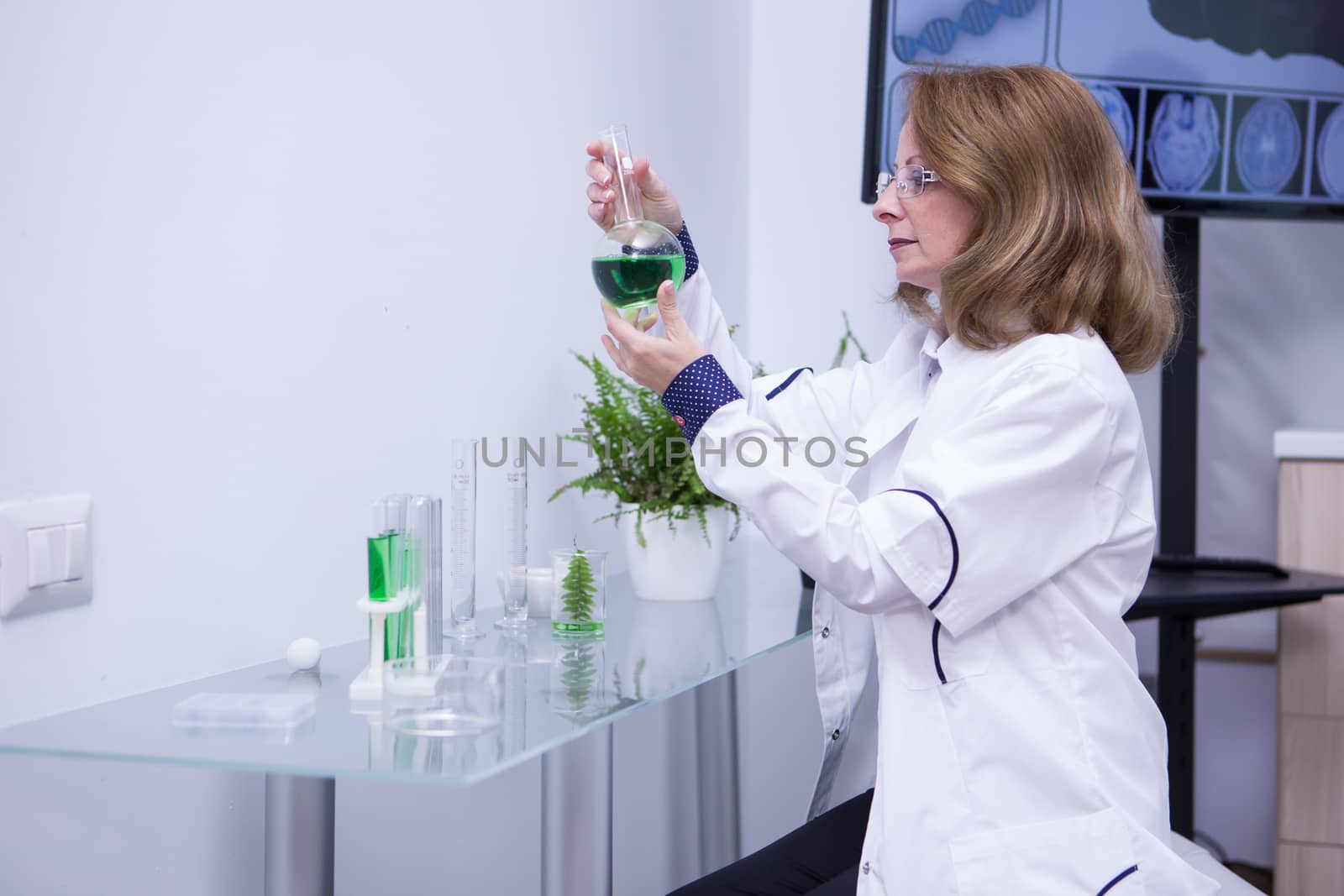 Mature female biologist looking at a green solution in her research lab. Adult scientist.