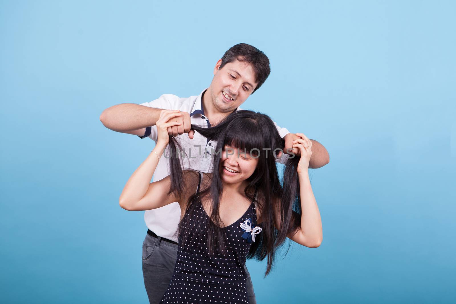Caucasian young man teasing his asian girlfriend pulling her hair. Interracial couple.