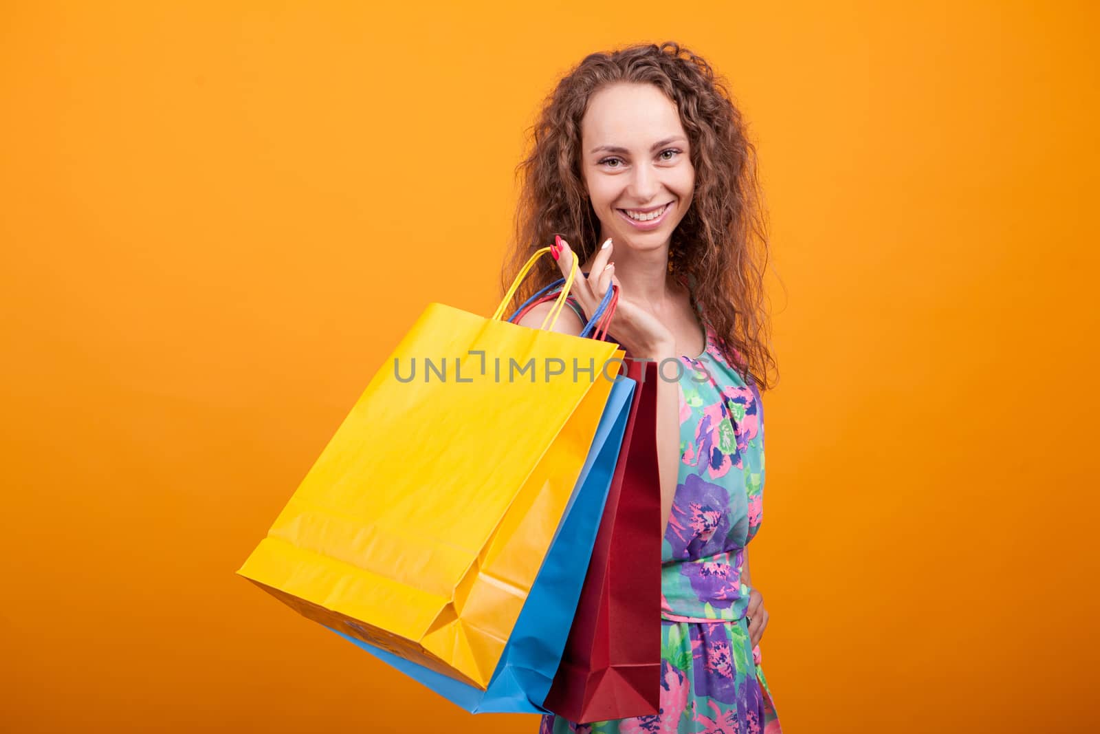 Stylish caucasian woman smiling and holding shopping bags over orange background.