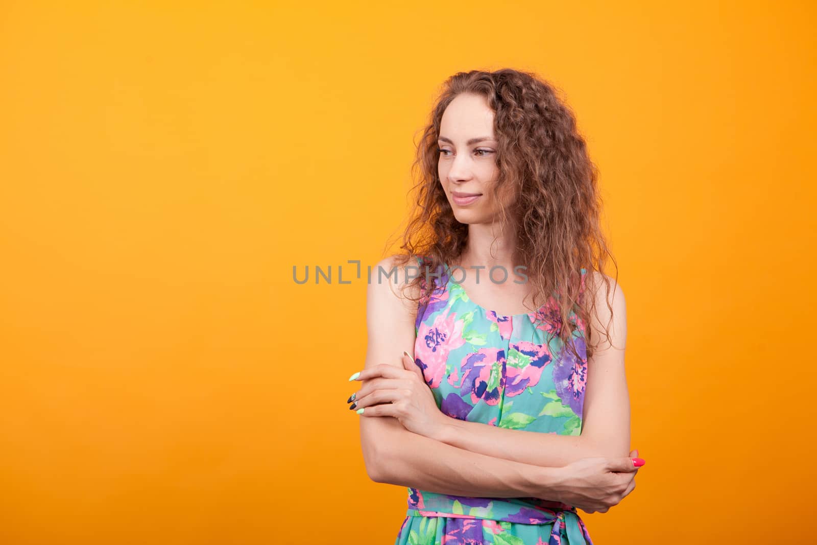 Young woman posing in studio keeping her arms corssed over orange background.