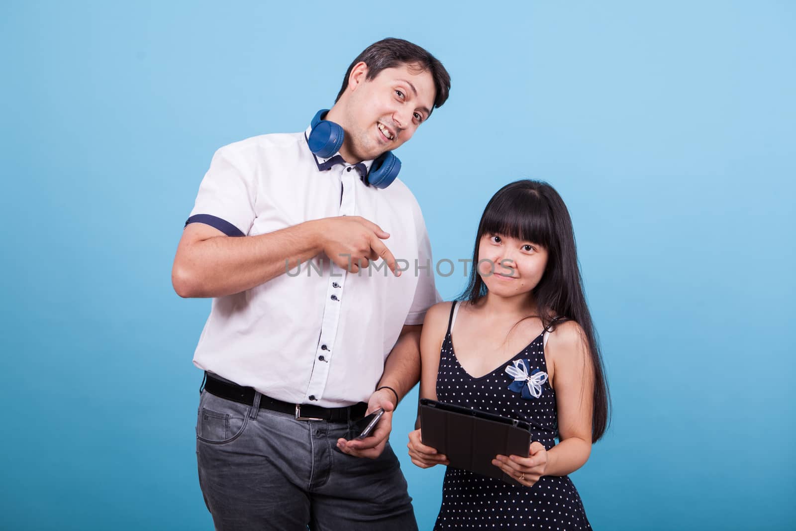 Asian girlfriend holding tablet and caucasian boyfriend pointing at it in studio. Interracial couple.