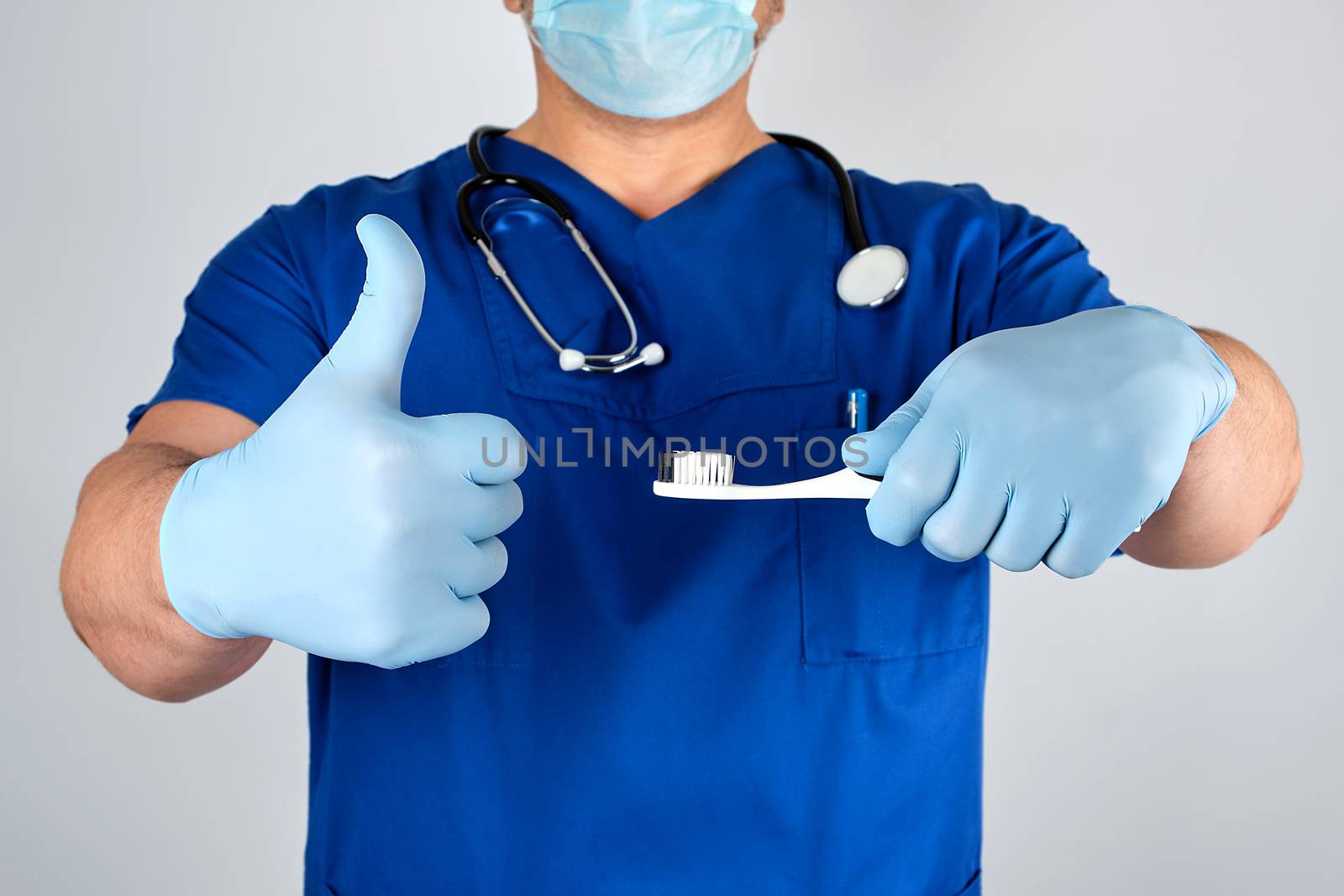 Doctor in sterile latex gloves and blue uniform holding a toothbrush, oral hygiene concept