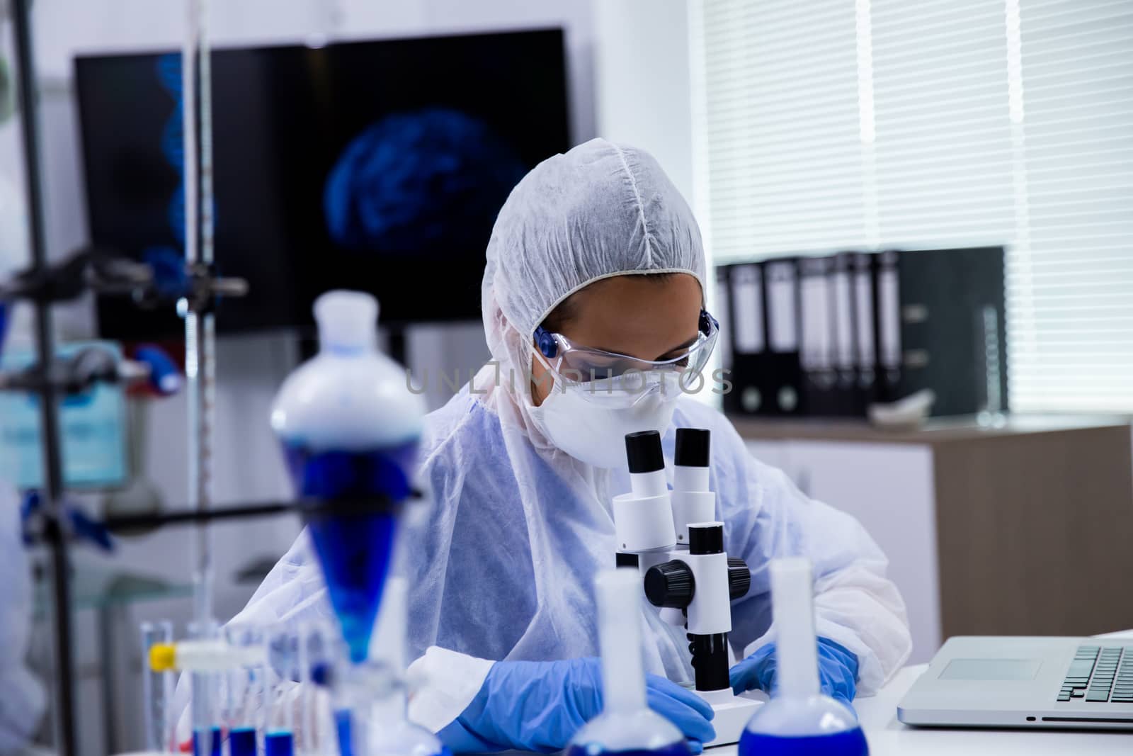 Female scientist analysing blue substance in a research laboratory on microscope.