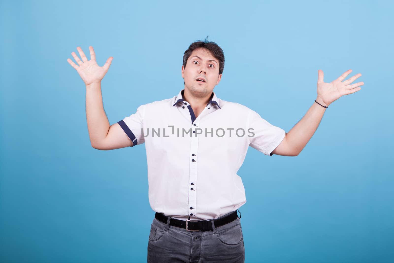 Confused caucasian young main riasing his hands in the air. Male in white shirt.