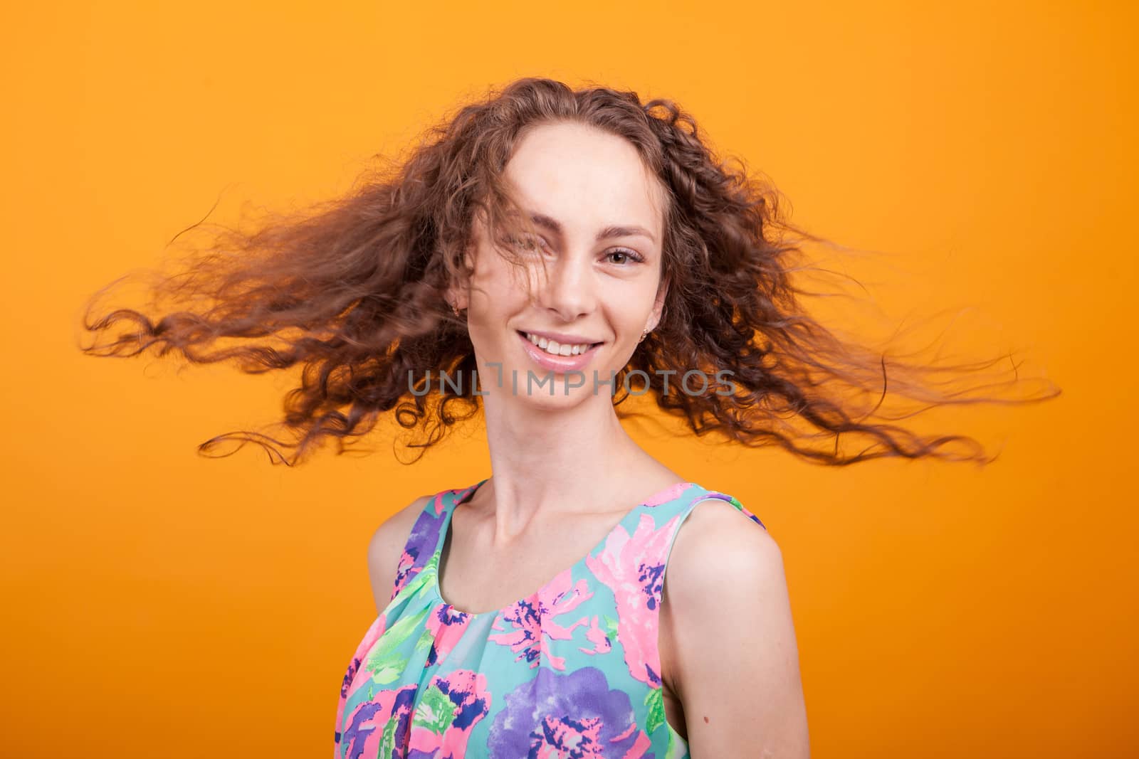 Gorgeous caucasian womam shaking her hair over orange background in studio wearing a pretty dress.