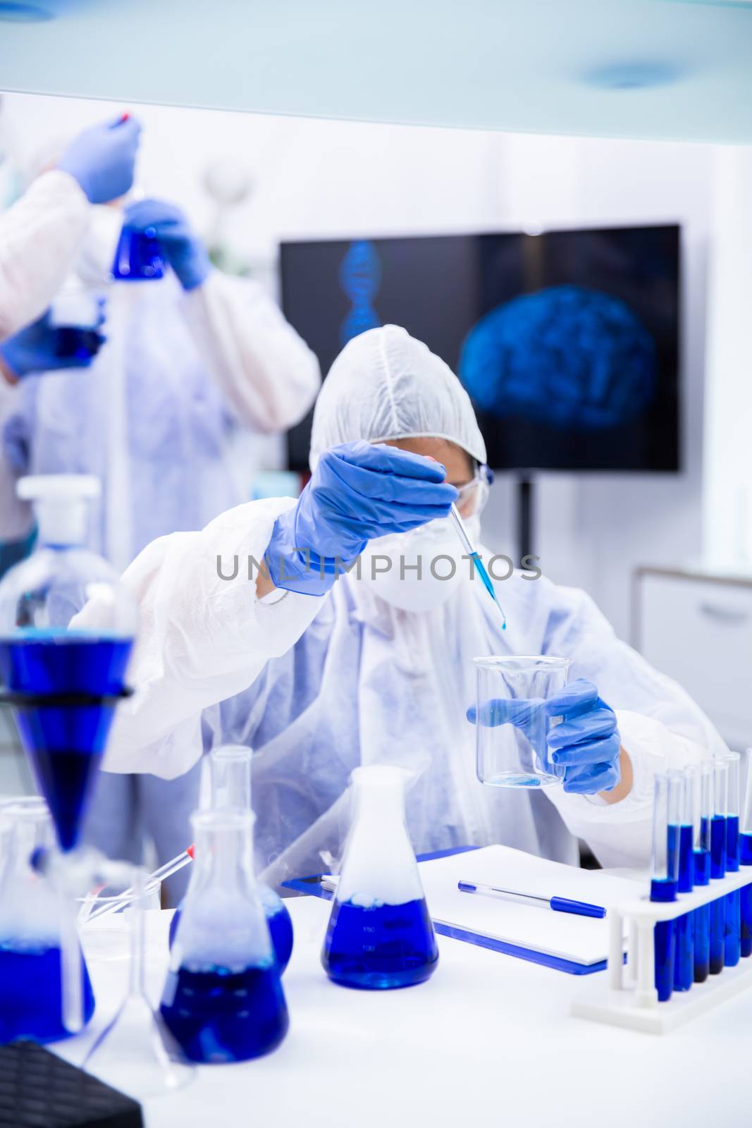 Chemist dripping from the pipette a blue liquid into a container. Surrounded by containers and container swith blue liquid