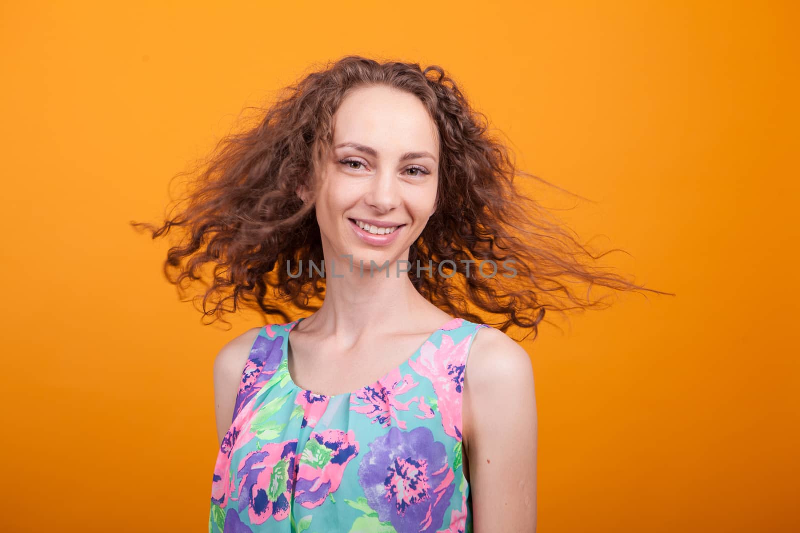 Beautiful woman portrait smiling and shaking her curly hair in studio over orange background.