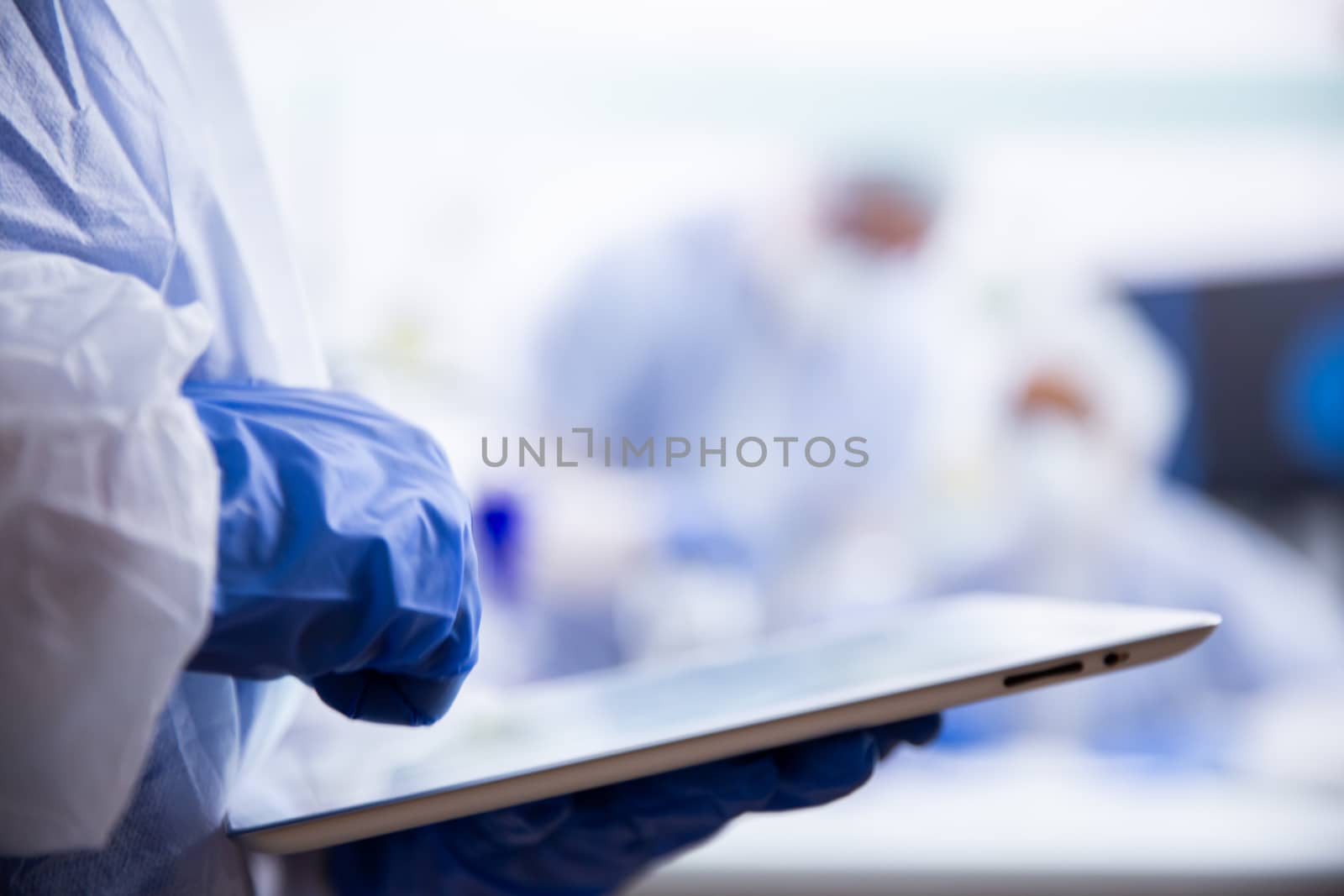The chemist in blue gloves uses a tablet that holds it in his hand. Close up