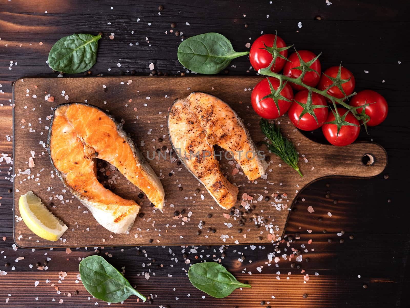 Top view of salmon spread on a wooden bottom and with some spinach leaves around. Salt and pepper together with tomatoes