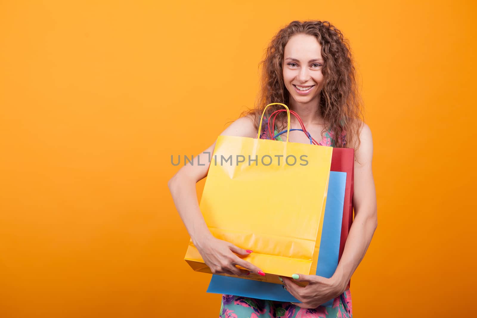 Joyful young lady smiling with shopping bags in her hands. Stylish caucasian woman over orange background.