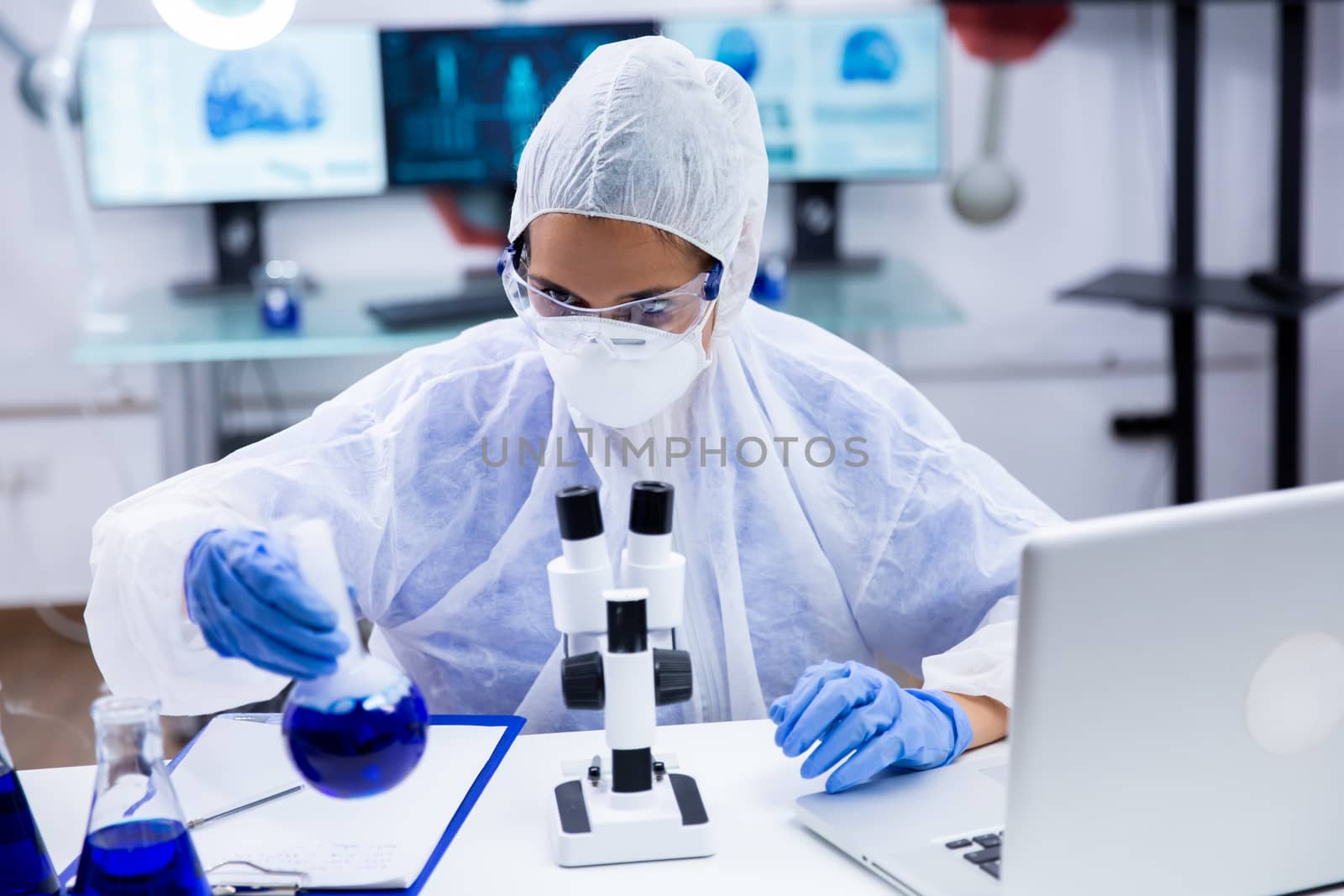 Caucasian Scientist sitting down shakes a tube with a blue substance. Medical equipment