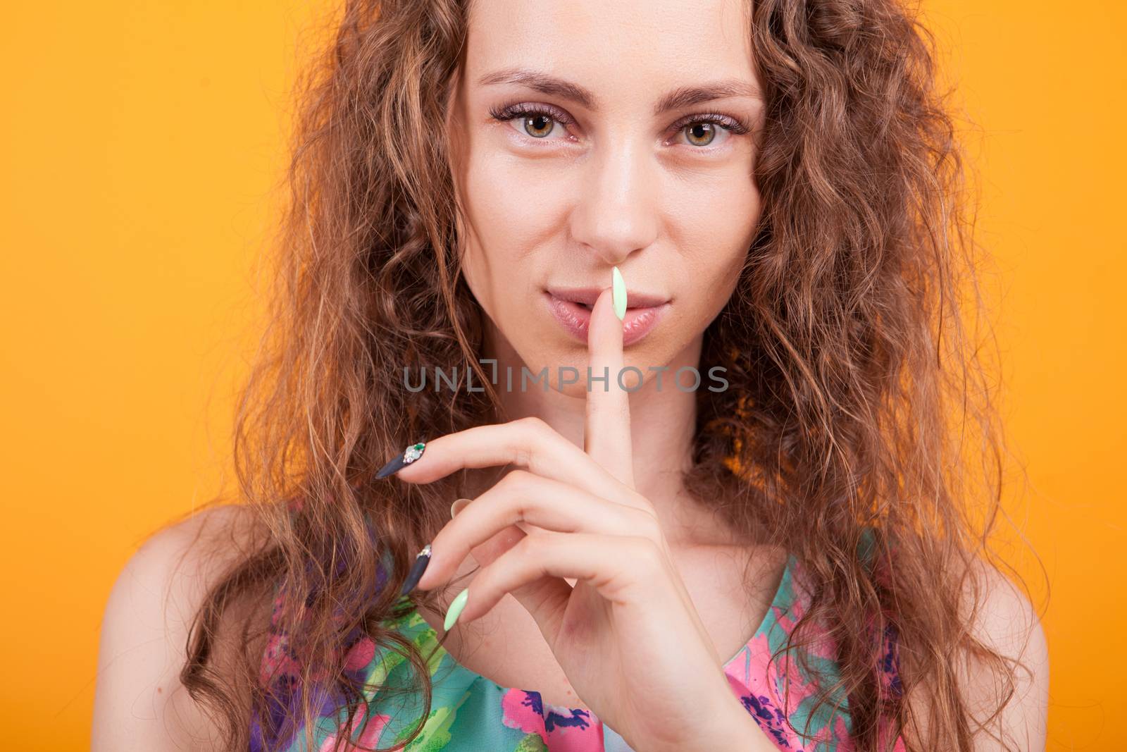 Young woman close up portrait making shh hand gesture in studio over orange background.