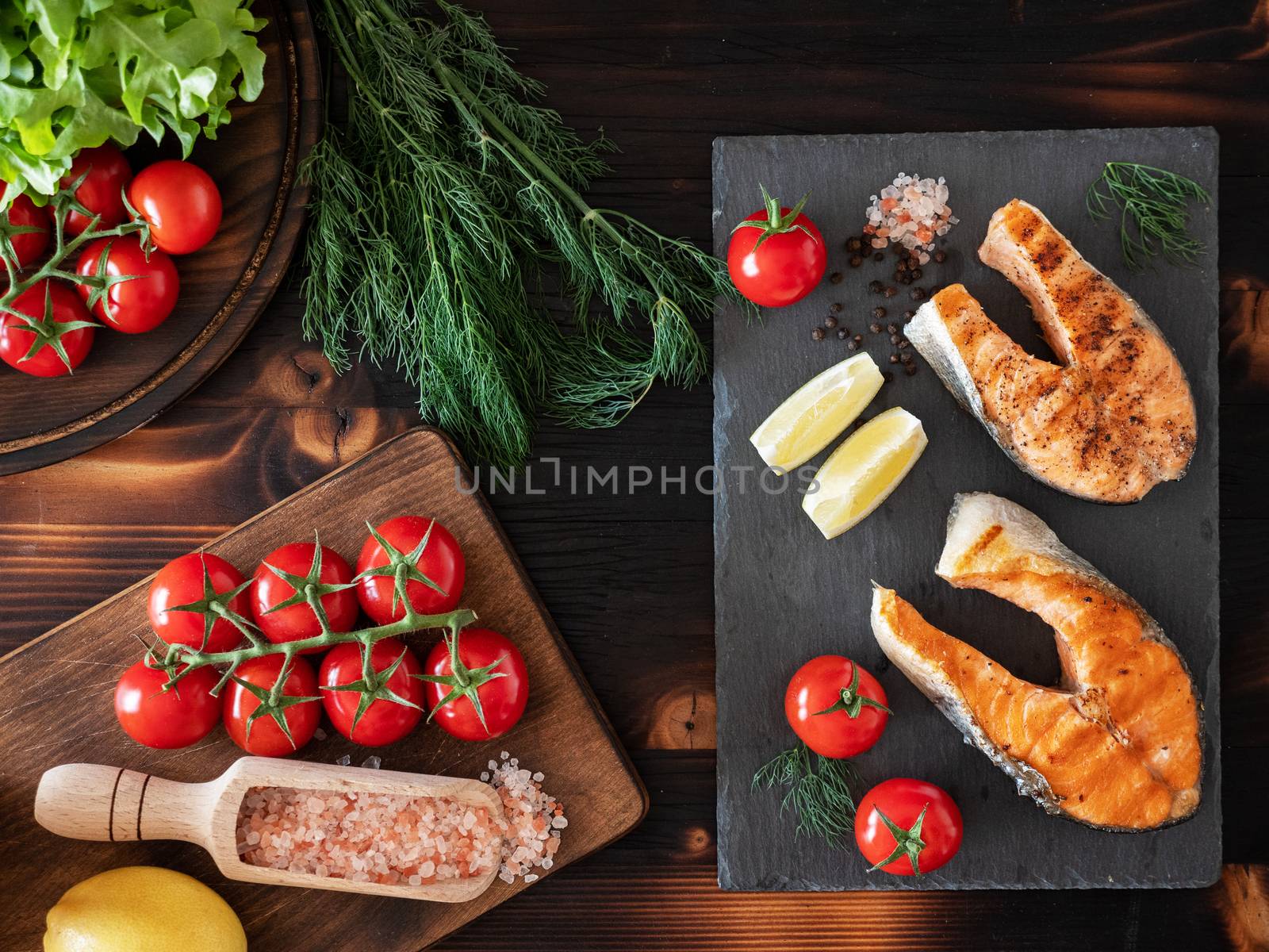 Top view of cooked salmon rings arranged on stone countertops next to cherry tomatoes, salad and lemon