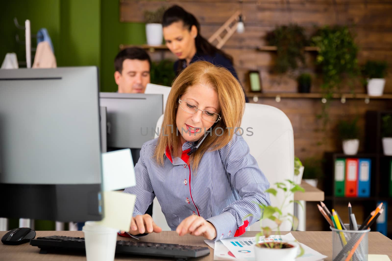 Middle female typing while having a serios conversation on her phone. Young female talking with her colleague in the background.