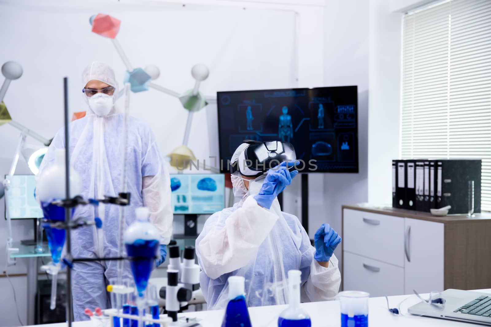Female scientist wearing virtual reality glasses pointing,. Test tubes with smoking blue liquid.