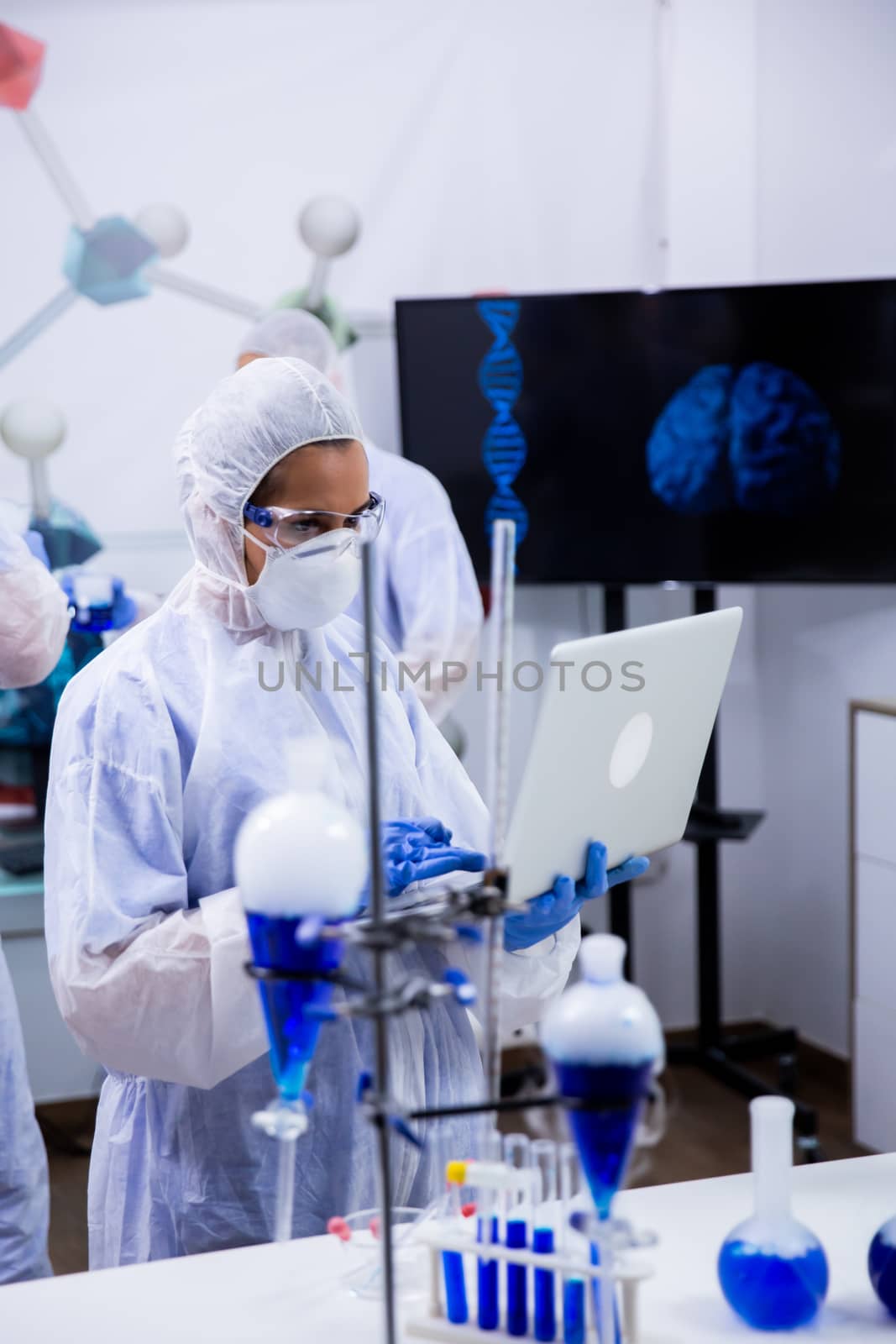 Scientist typing on her computer data from exeperiments with smoking blue solution in test tubes.