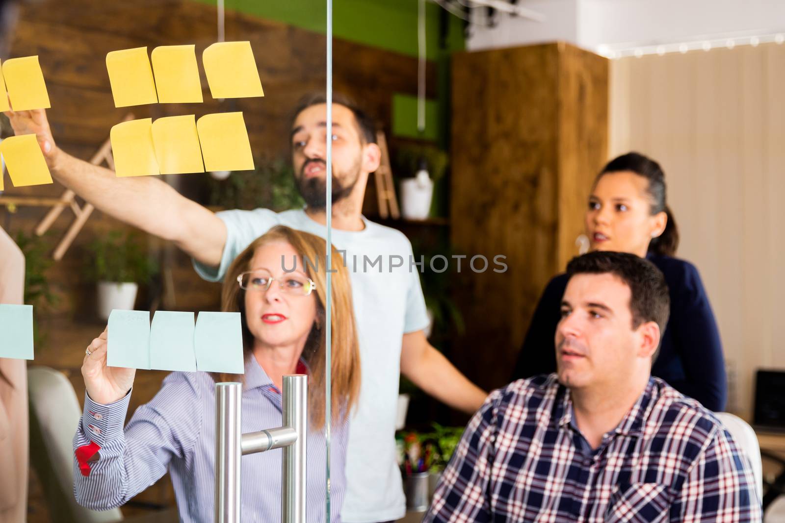 Group of young entrepreneurs looking at sticky notes on a glass window in modern office