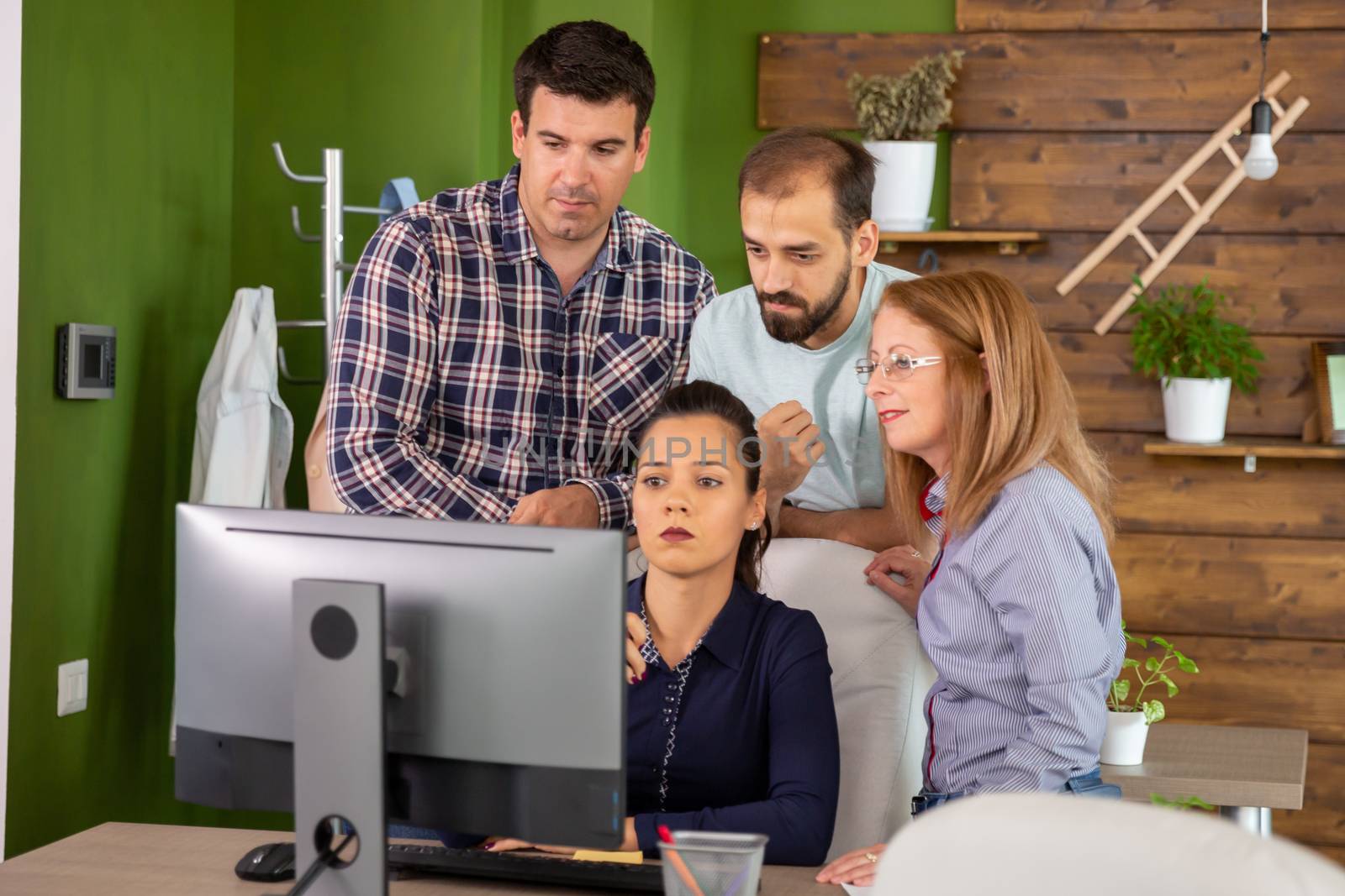 Team gathered behind their manager looking into computer monitor. Young manager.