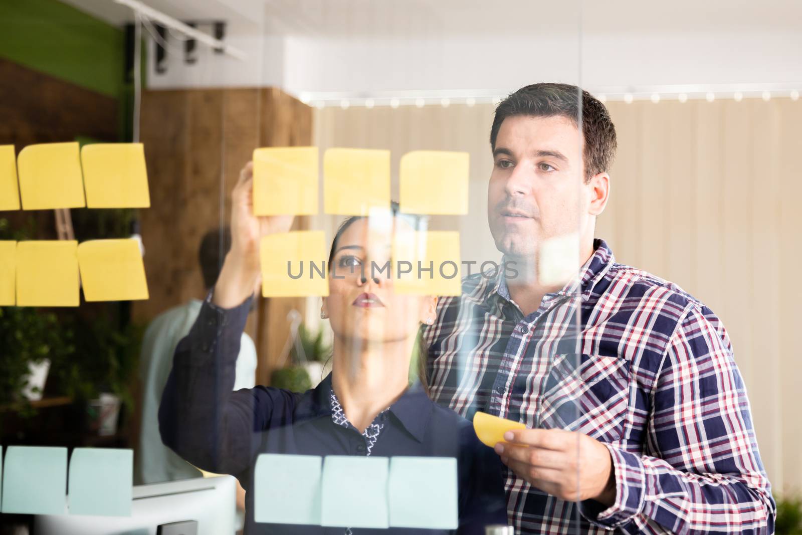 Two entrepreneurs looking at sticky notes on a glass window in modern office