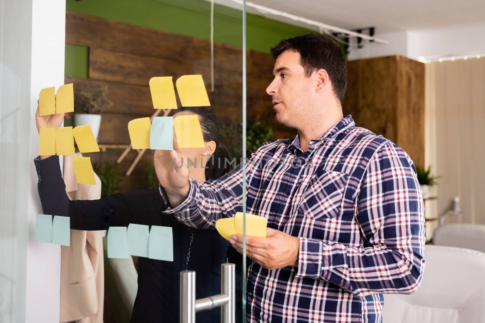 Two entrepreneurs planning a new strategy. They are looking at sticky paper on glass door