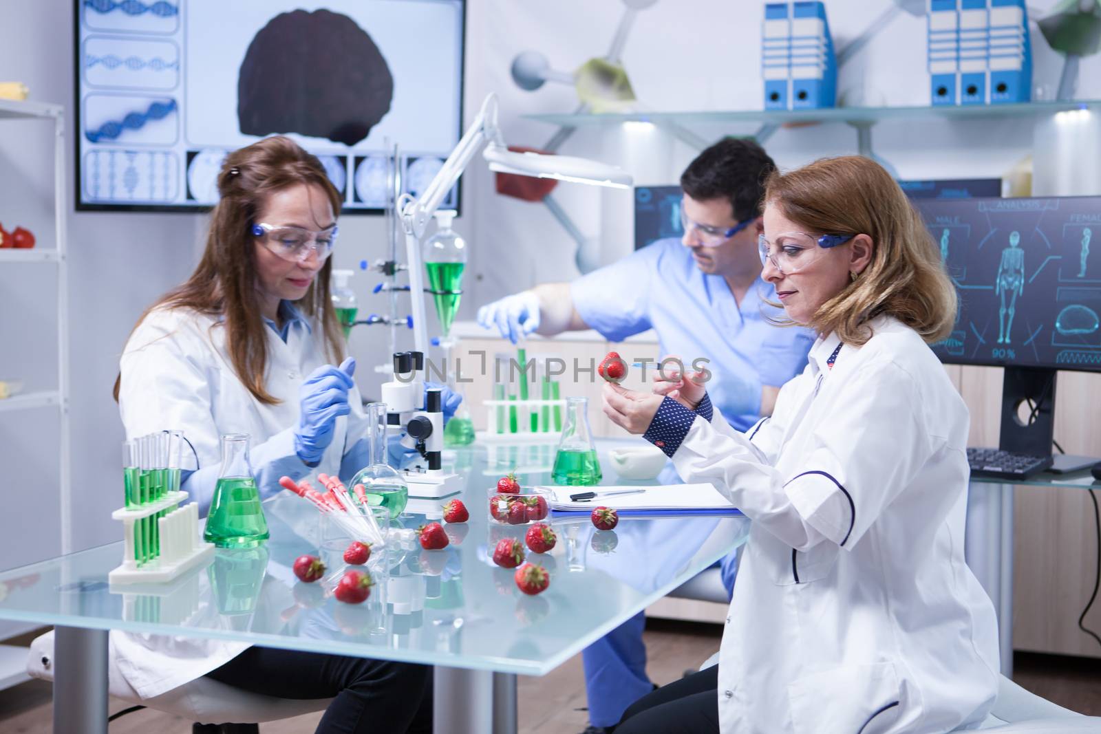 Caucasian woman with protection glasses doing scientific test on strawberries. Processing strawberries.
