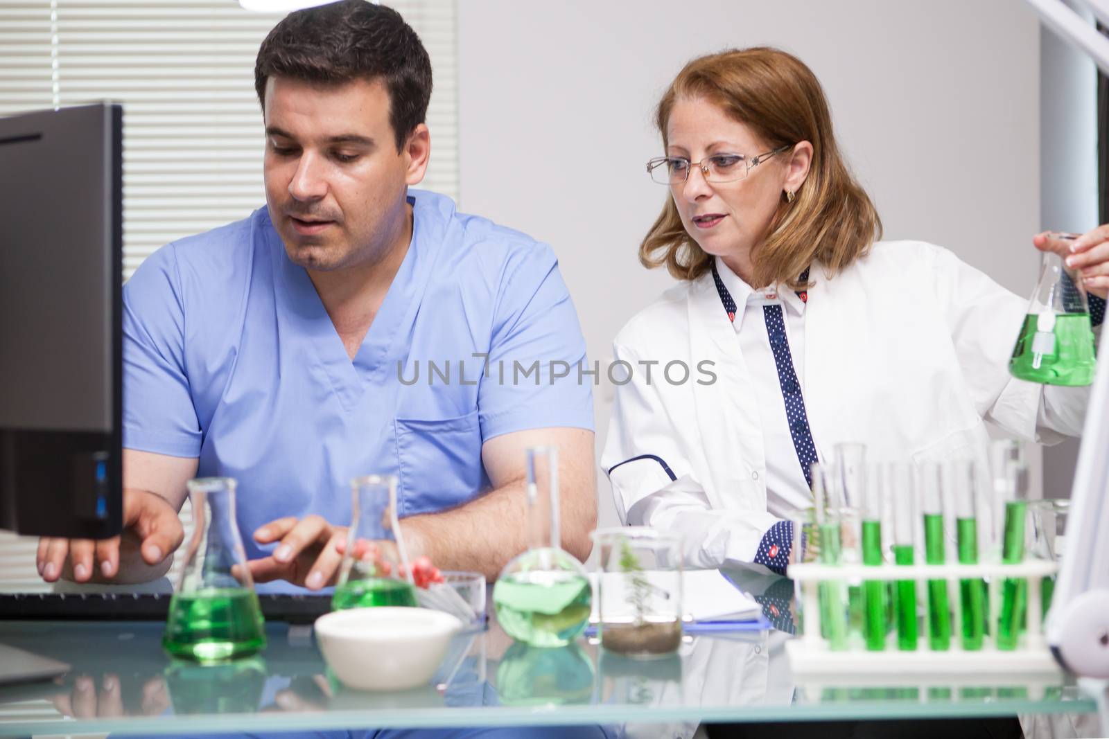 Photo of young assistant introducing the data that the leading scientist it's telling him. Research lab. Microbiological analysis.