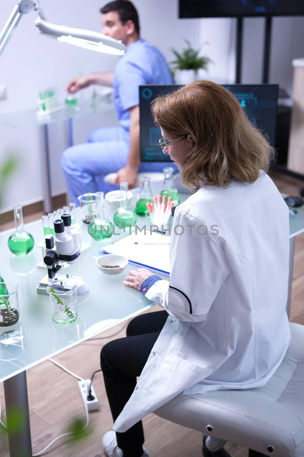 Middle age female scientist taking a sample of soil for for microscope analysis. Young biologist working in the background.