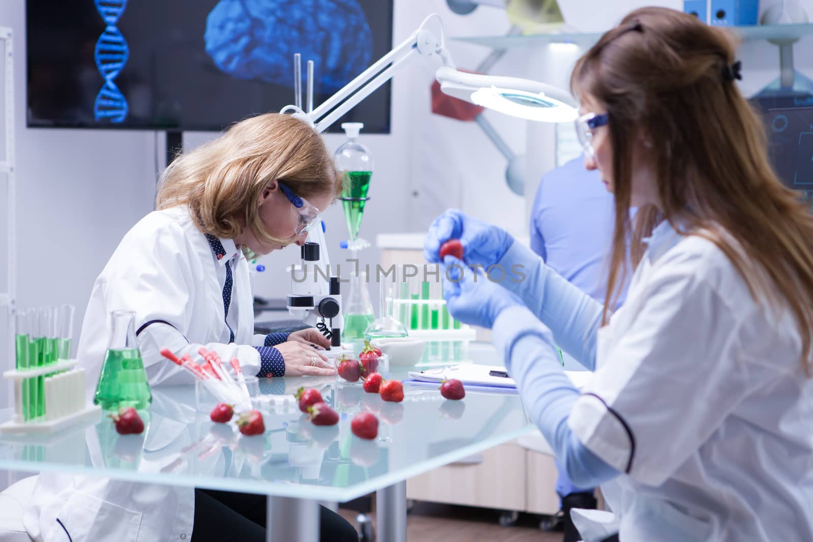 Two female scientist working together in research lab for food. Test tubes. Tests on strawberries.