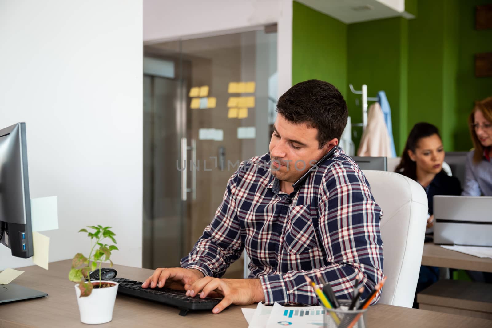 Man in start-up company office talking on the phone. His colleagues are working in the background