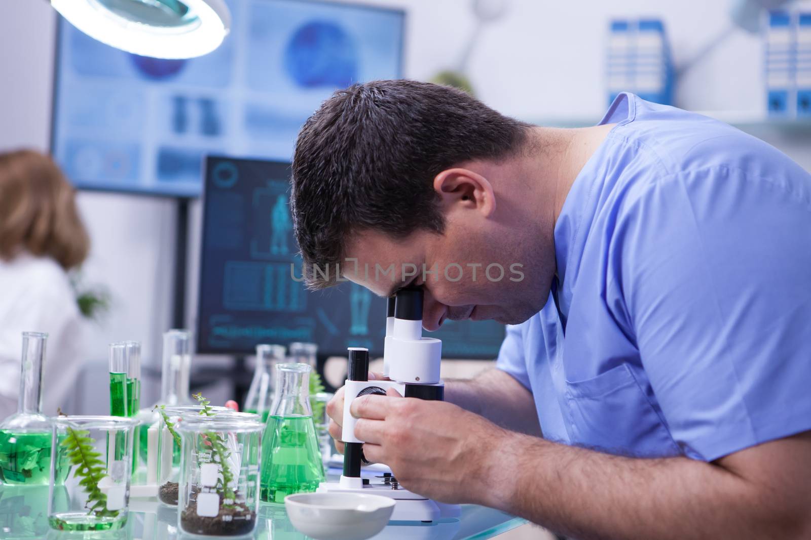 Scientist man looking through microscope after viruses in a research lab for agriculture industry. Test tubes.