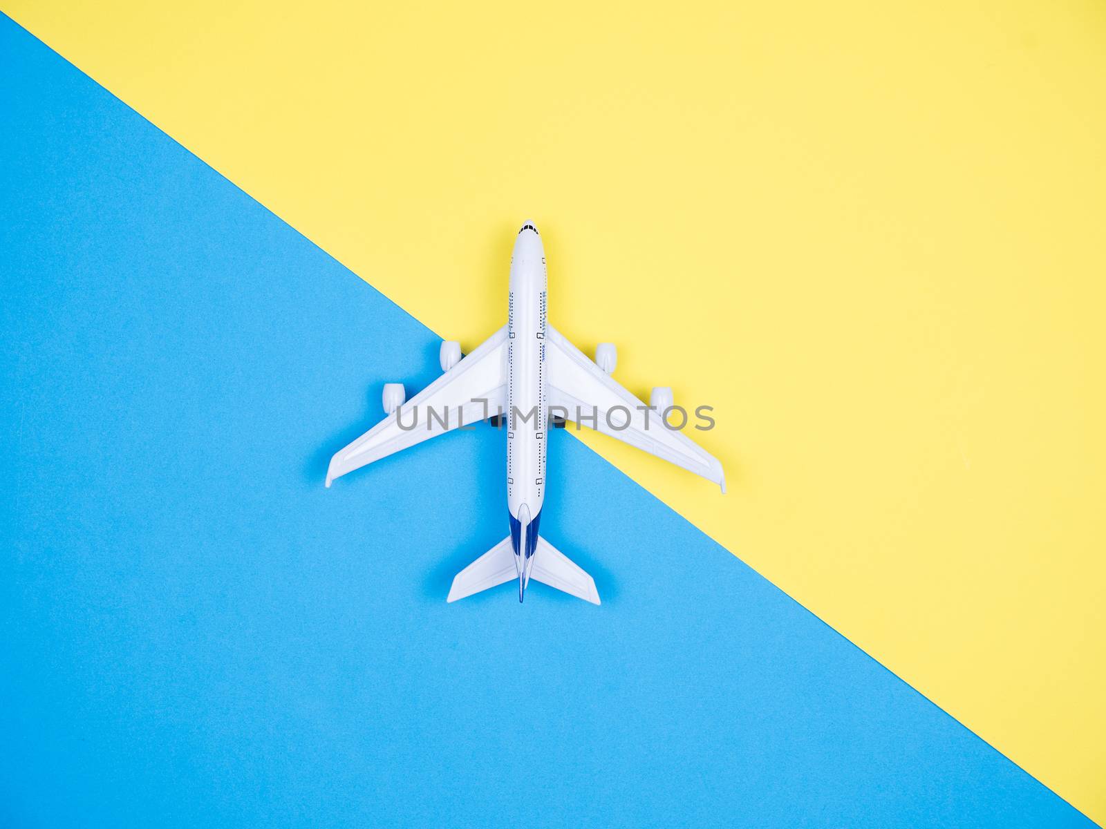 Top view of white toy plane over yellow and blue background. Copyspace available.