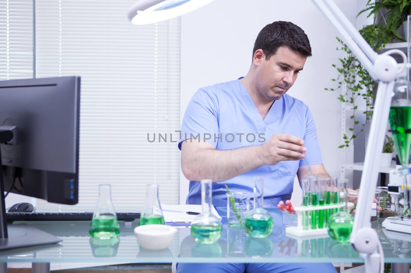 Young caucasian scientist man taking a sample of solution from a test tube. Microbiology lab.