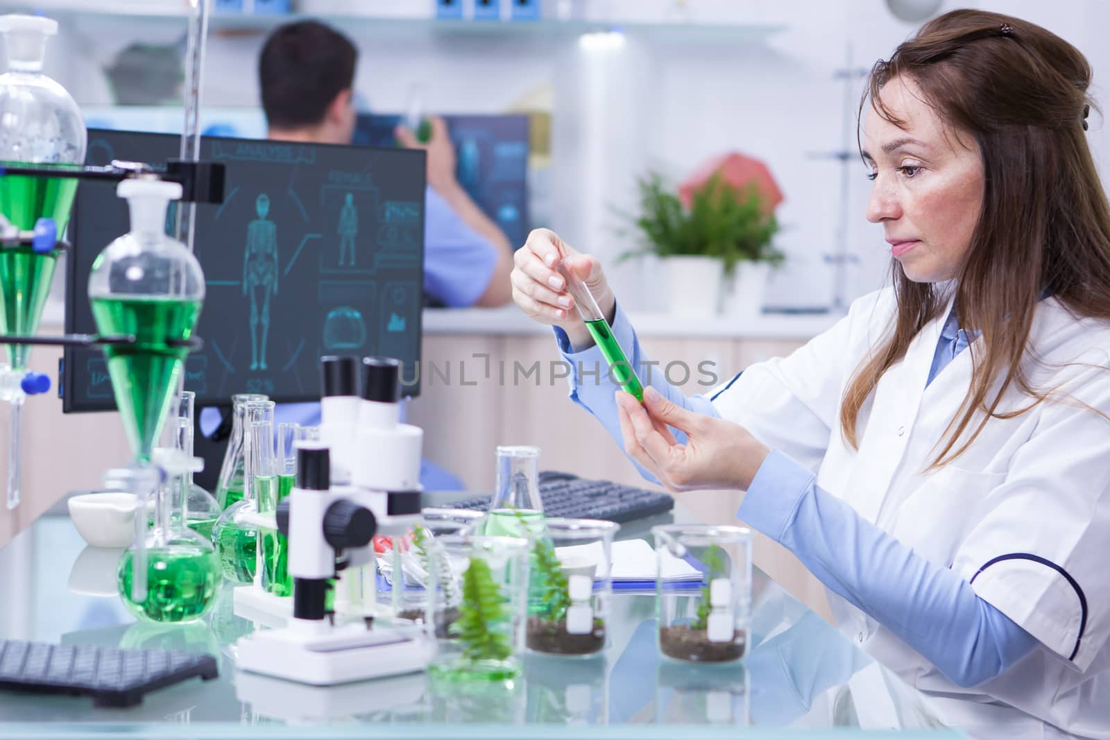 Side view of female scientist doing research on plants holding a green solution in a test tube. Female bioligist.