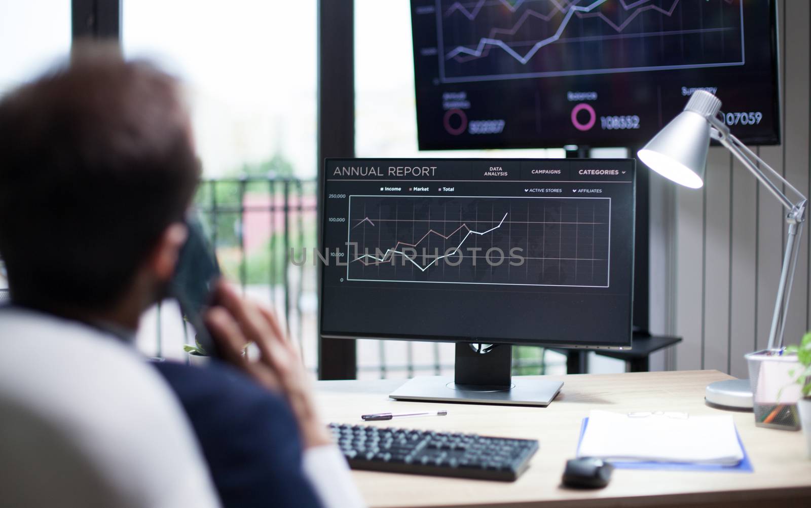 Young marketing expert looking at grafics on monitor and having a business conversation on his phone. Handsome young man.