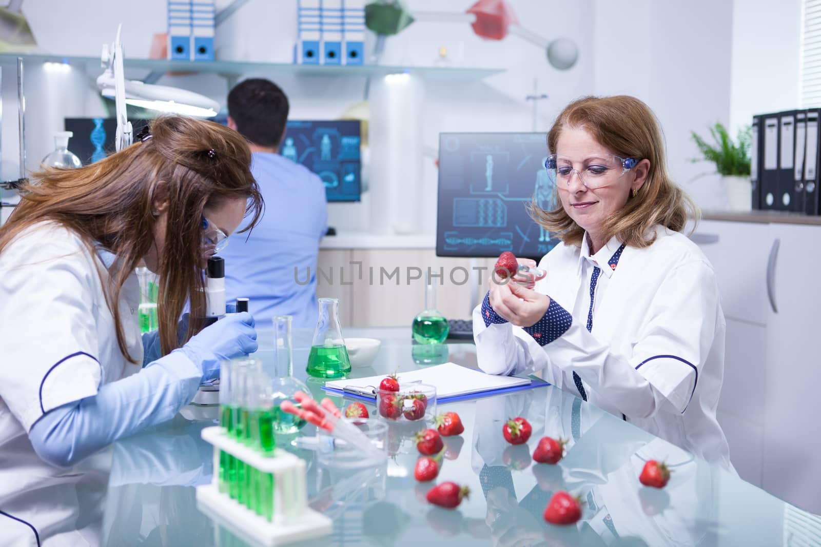 Middle age female in white coat working as scientist in a lab research. Science test on strawberries.